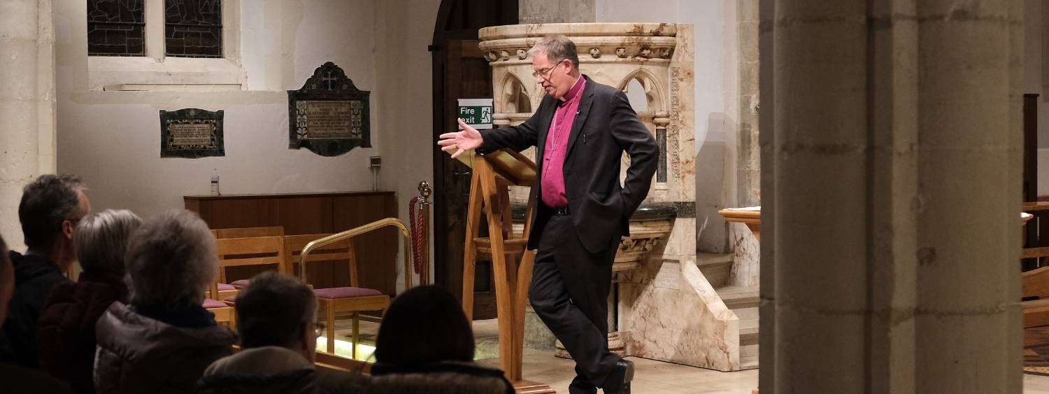 The Bishop of Oxford standing leaning on a lectern talking to a seated congregation